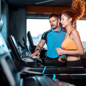 pretty female exercising on running track in gym with instructor